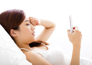 young woman looking smart phone with tired eyes on the bed